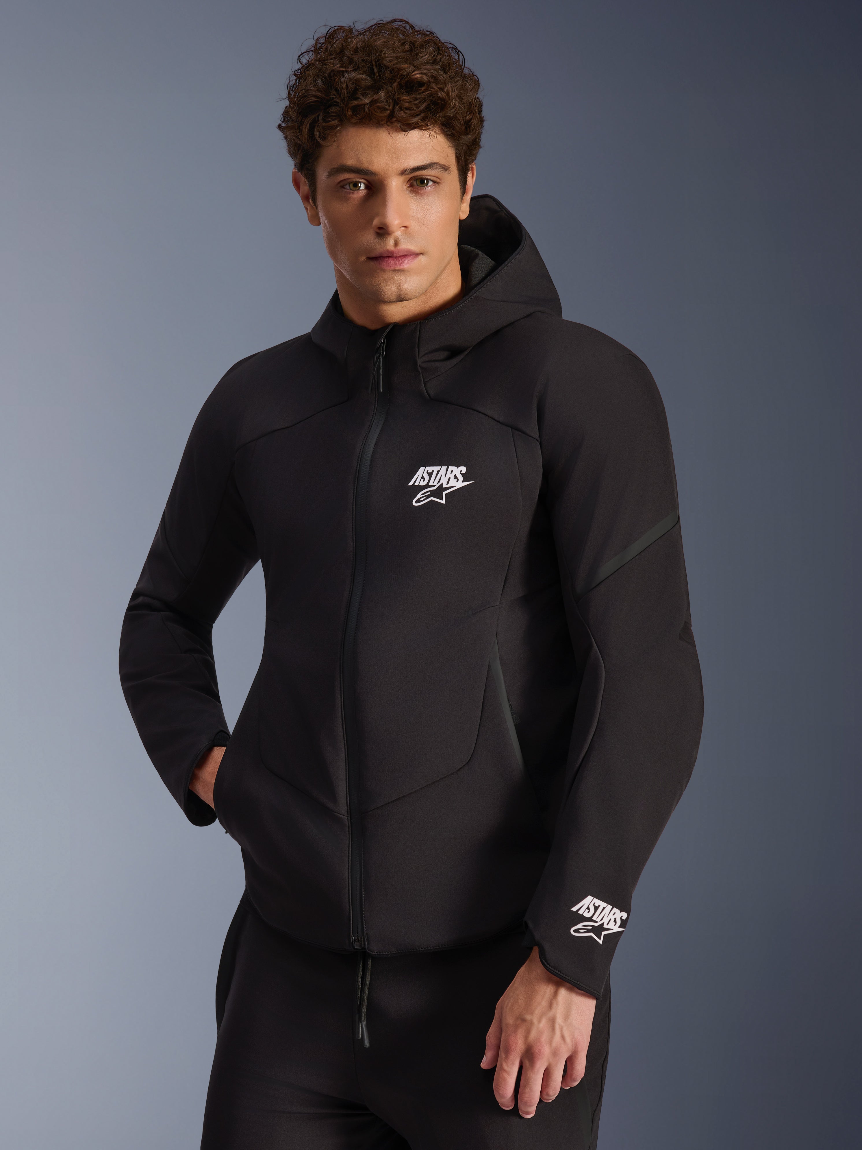 Alpinestars Aeroshell Waterproof Jacket, felpa da moto in softshell nera, logo ASTARS bianco sul petto e sul polsino, design elegante con cappuccio integrato e cerniera impermeabile, abbigliamento moderno d'ispirazione sportiva per la guida urbana