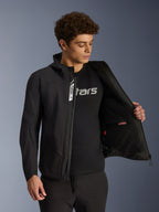 Giacca Alpinestars Aeroshell Waterproof, giacca da moto in softshell nero, aperta per mostrare la tasca interna e la fodera, indossata da un modello con t-shirt nera con logo, design con cappuccio per la guida urbana casual e lo stile street.