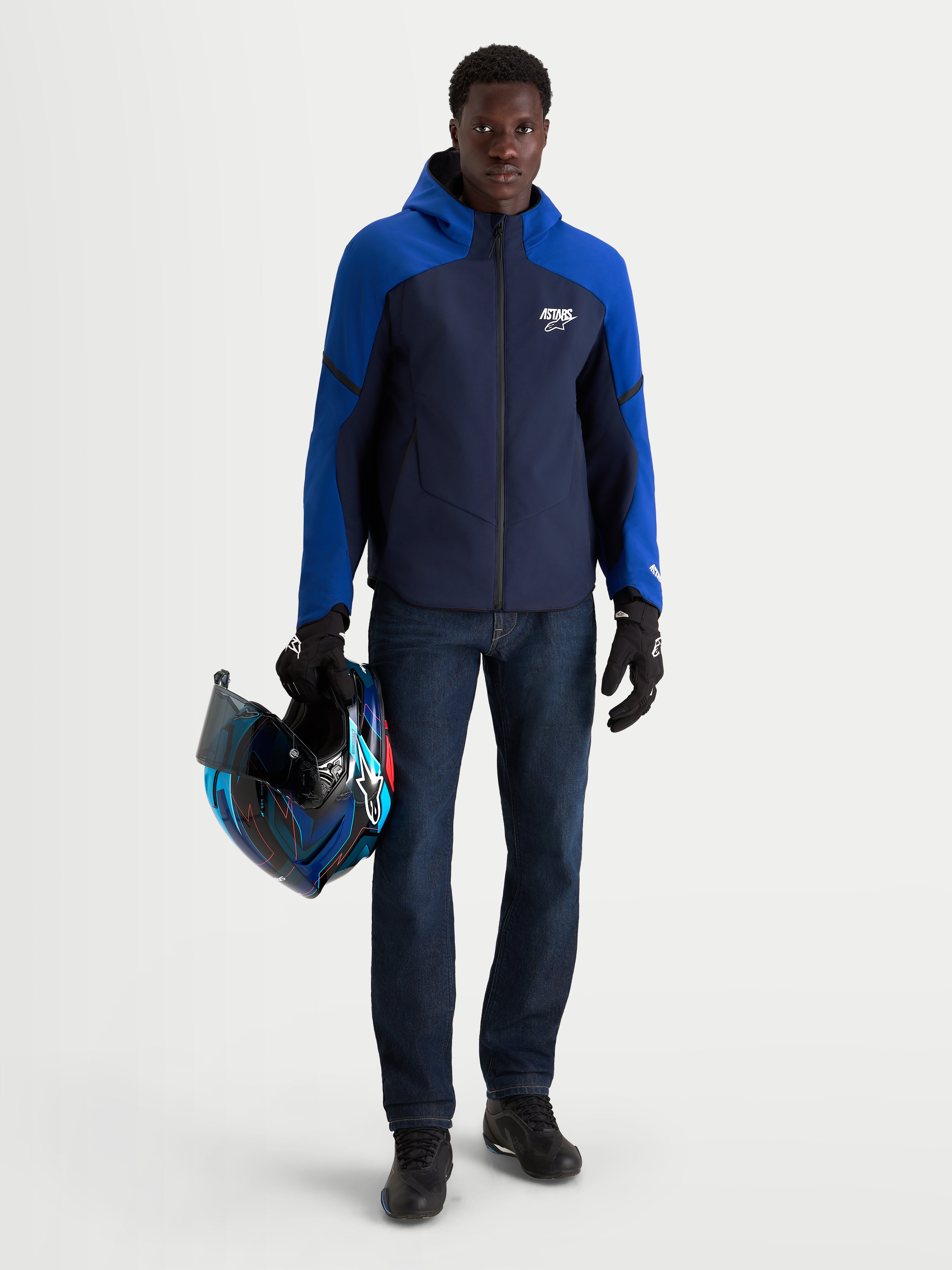 Alpinestars Aeroshell Wp Giacca, giacca da moto sportiva da uomo in blu navy e blu brillante con cappuccio, indossata da un modello che tiene un casco abbinato