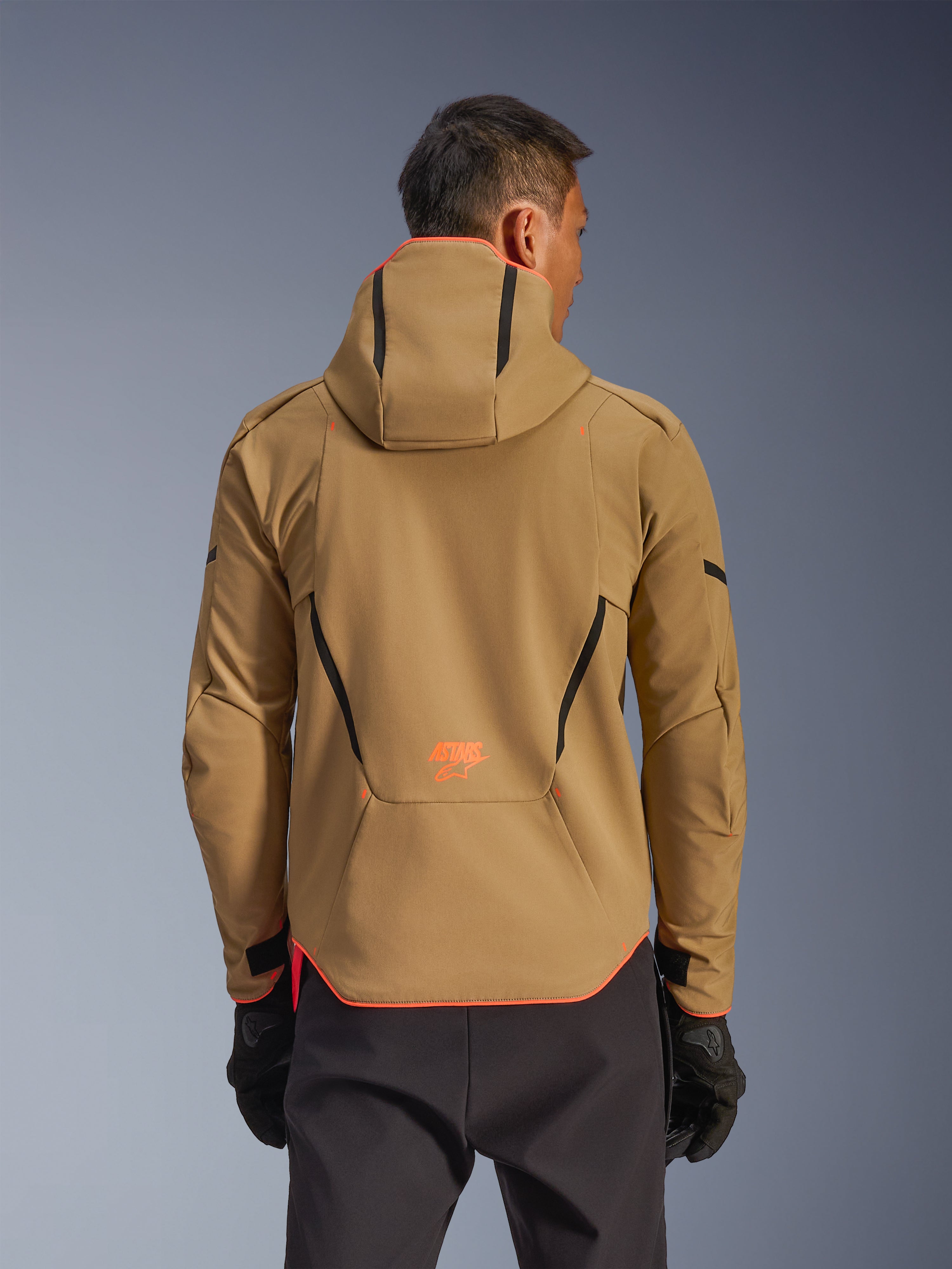 Giacca impermeabile Alpinestars Aeroshell, Dark Khaki e Arancione Fluo, vista posteriore con design a felpa con cappuccio e profili arancioni su cappuccio e orlo, logo arancione sulla parte bassa della schiena, indossata con guanti neri, abbigliamento da moto softshell sportivo crossover.