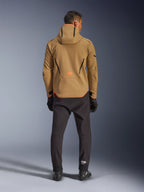 Alpinestars Aeroshell Waterproof Jacket in Dark Khaki Black Orange Fluo, vista posteriore di un uomo che indossa la giacca softshell con cappuccio, con profili neri e logo arancione, abbinata a pantaloni tecnici e guanti neri