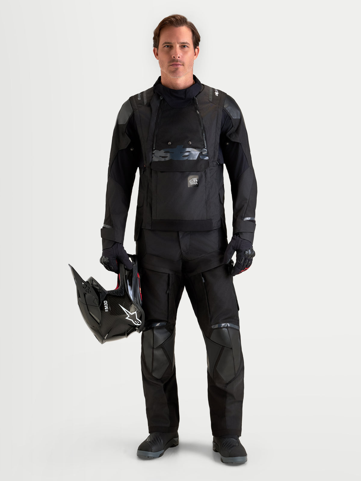 Alpinestars Harok V 2 Drystar Giacca, giacca da moto adventure da uomo in nero, indossata con pantaloni da moto coordinati mentre tiene un casco, con costruzione impermeabile