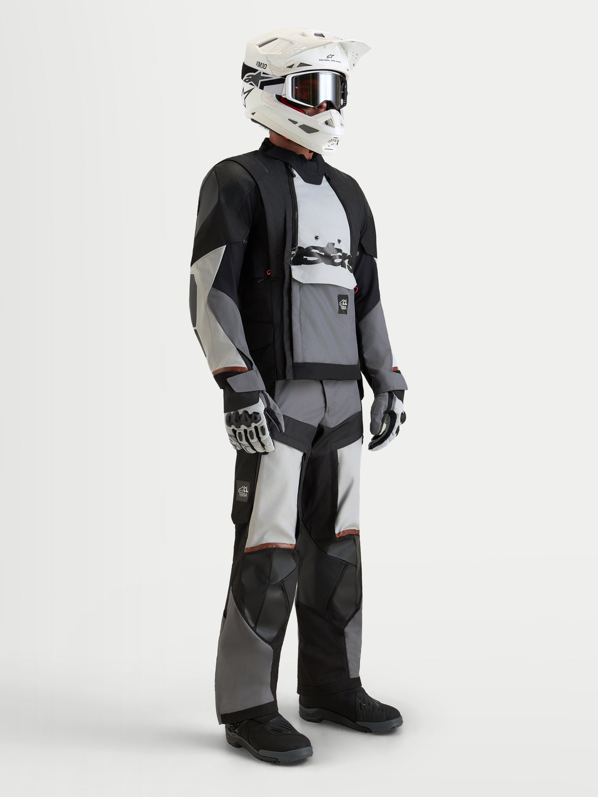 Alpinestars Harok V2 Drystar Giacca, giacca da moto adventure da uomo in grigio scuro, grigio ghiaccio e nero, indossata con equipaggiamento coordinato, casco e guanti, con ventilazione modulare all-terrain e costruzione impermeabile