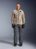 Giacca Alpinestars Borrego Drystar®, giacca da moto adventure, grigio Warm Gray, indossata da un modello con pantaloni da guida grigio scuro e guanti neri, con numerose tasche cargo e una robusta costruzione in tessuto dal classico look in tela cerata