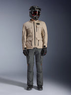 Giacca Alpinestars Borrego Drystar® in Warm Gray, giacca da moto adventure con quattro tasche cargo anteriori, abbinata a pantaloni da guida grigio scuro, casco off-road nero e guanti neri, caratterizzata da un robusto look in tela cerata