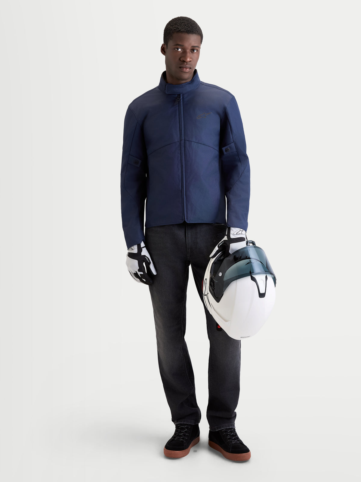 Alpinestars C 1 Waterproof Giacca, giacca da moto urbana contemporanea da uomo in blu scuro, vista frontale su un modello che indossa guanti coordinati e tiene un casco bianco, abbigliamento da moto impermeabile