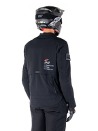 Vista posteriore di un pilota che indossa la giacca Alpinestars AMT-8 Stretch Drystar® XF in nero, caratterizzata dal marchio 'AMT Alpinestars Motion Technology' sulla schiena e ventilazione tecnica con cerniera, abbinata a casco da moto e guanti neri