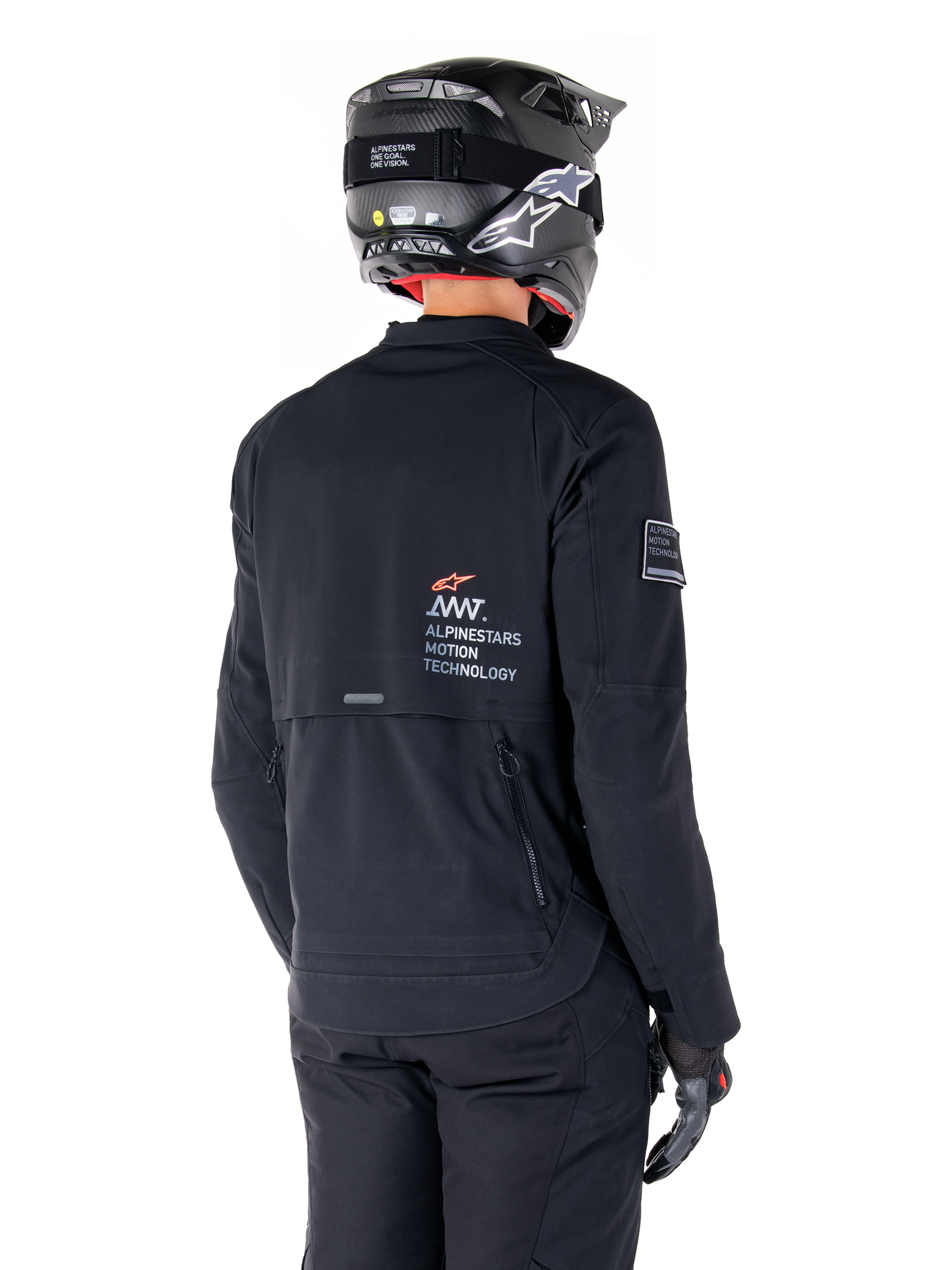 Vista posteriore di un pilota che indossa la giacca Alpinestars AMT-8 Stretch Drystar® XF in nero, caratterizzata dal marchio 'AMT Alpinestars Motion Technology' sulla schiena e ventilazione tecnica con cerniera, abbinata a casco da moto e guanti neri