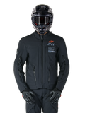 Giacca Alpinestars AMT-8 Stretch Drystar® XF, giacca da moto nera, con logo Alpinestars arancione e marchio AMT grigio, collo alto con cerniera frontale e prese d'aria, indossata con casco e guanti neri, abbigliamento protettivo per adventure touring