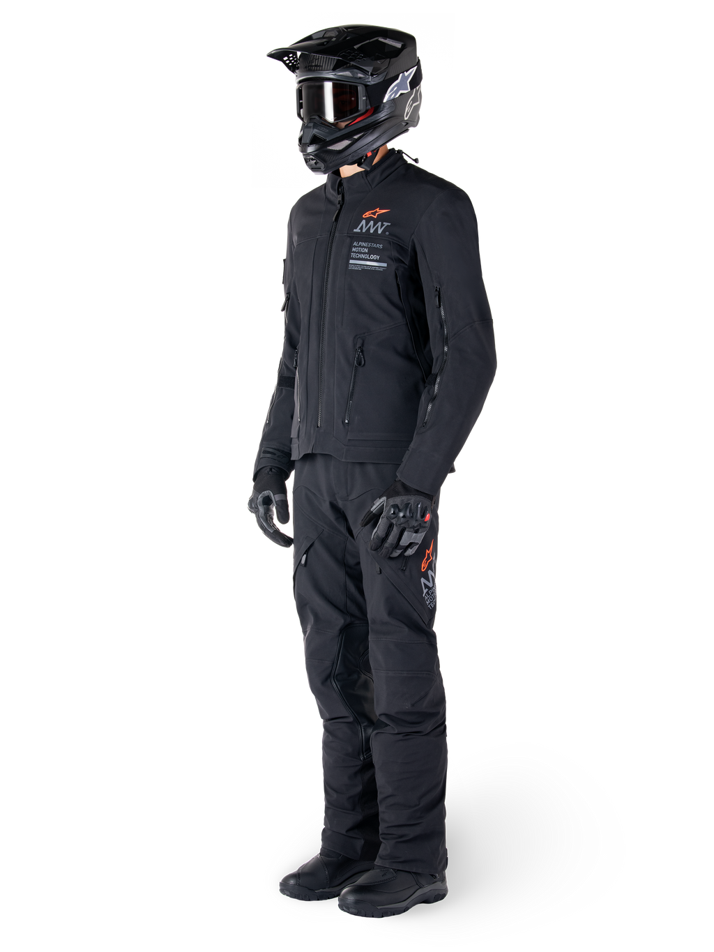 Alpinestars AMT-8 Stretch Drystar® XF Jacket, giacca da moto adventure, nero, indossata con pantaloni coordinati, casco e guanti, con marchio Alpinestars Motion Technology e accenti arancioni, struttura elasticizzata resistente per la guida adventure