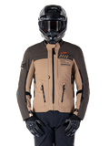 Giacca Alpinestars AMT-8 Stretch Drystar XF, giacca da moto adventure touring, cachi scuro e marrone scuro, con logo Astars arancione e cerniere nere, indossata con casco adventure e guanti neri, equipaggiamento da guida completo