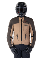 Giacca Alpinestars AMT-8 Stretch Drystar XF, giacca da moto adventure touring, cachi scuro e marrone scuro, con logo Astars arancione e cerniere nere, indossata con casco adventure e guanti neri, equipaggiamento da guida completo