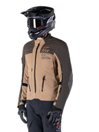 Giacca Alpinestars AMT-8 Stretch Drystar® XF, giacca da moto adventure, marrone scuro e dark khaki, indossata con casco off-road nero e maschera, con logo Alpinestars Motion Technology e prese d'aria con cerniera.