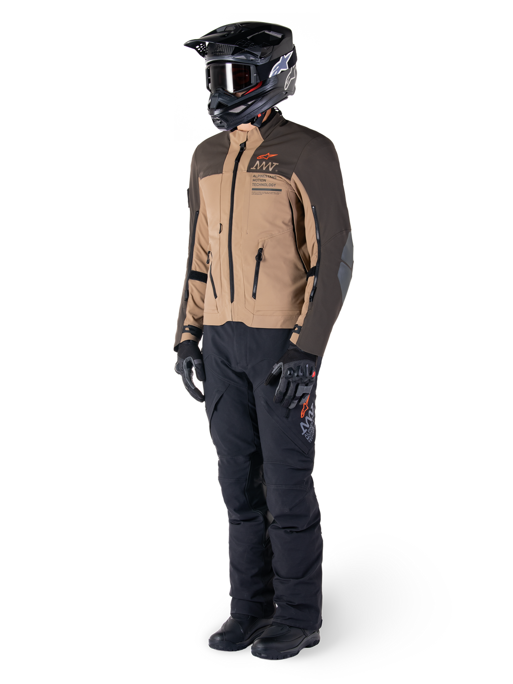 Pilota adventure con equipaggiamento completo, giacca Alpinestars AMT-8 Stretch Drystar® XF in marrone scuro e kaki scuro, abbinata a pantaloni adventure neri, casco, guanti e stivali neri, con logo AMT arancione e cerniere di ventilazione tecniche per il touring a lungo raggio