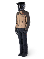 Pilota adventure con equipaggiamento completo, giacca Alpinestars AMT-8 Stretch Drystar® XF in marrone scuro e kaki scuro, abbinata a pantaloni adventure neri, casco, guanti e stivali neri, con logo AMT arancione e cerniere di ventilazione tecniche per il touring a lungo raggio