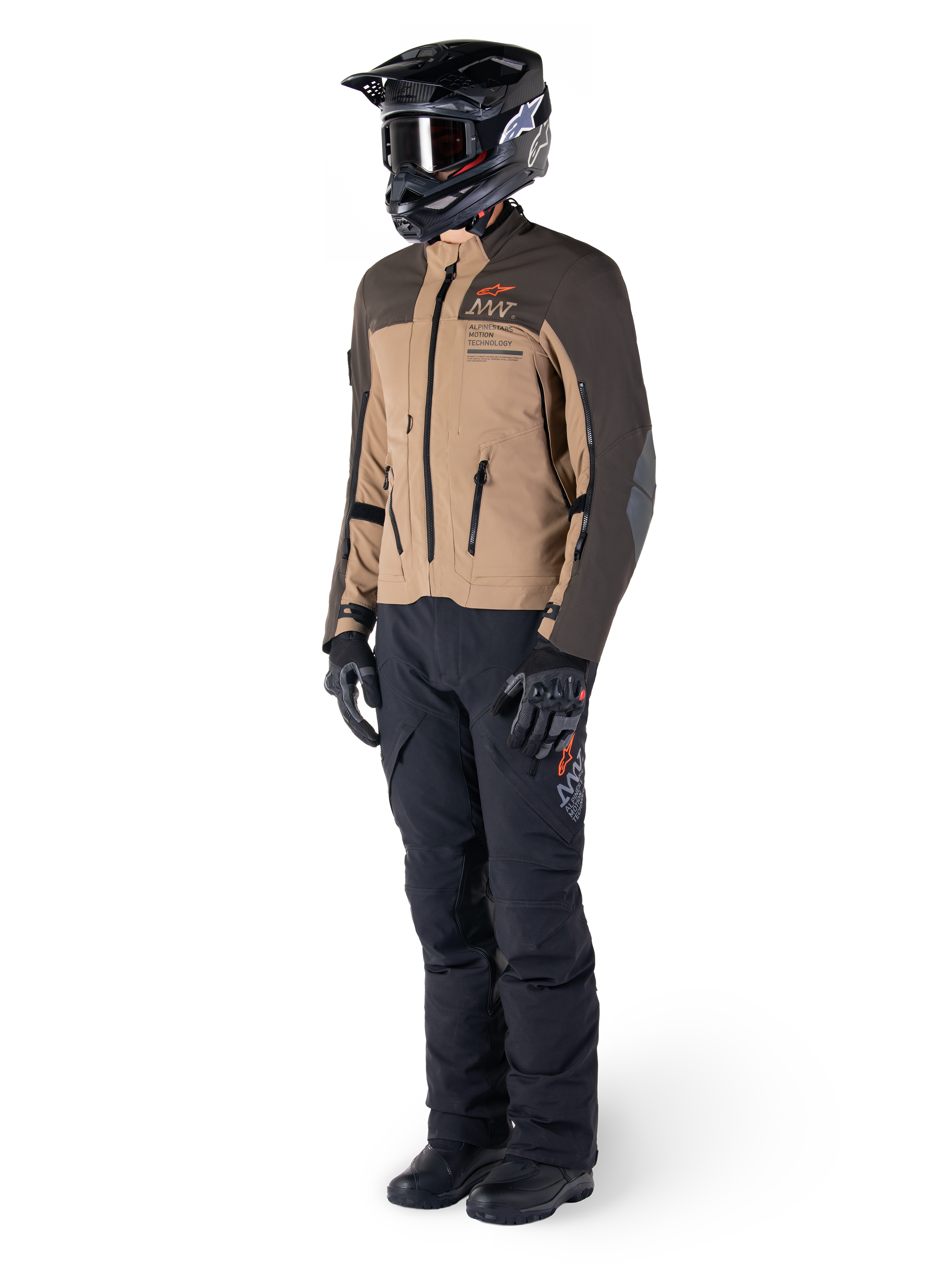 Pilota adventure con equipaggiamento completo, giacca Alpinestars AMT-8 Stretch Drystar® XF in marrone scuro e kaki scuro, abbinata a pantaloni adventure neri, casco, guanti e stivali neri, con logo AMT arancione e cerniere di ventilazione tecniche per il touring a lungo raggio