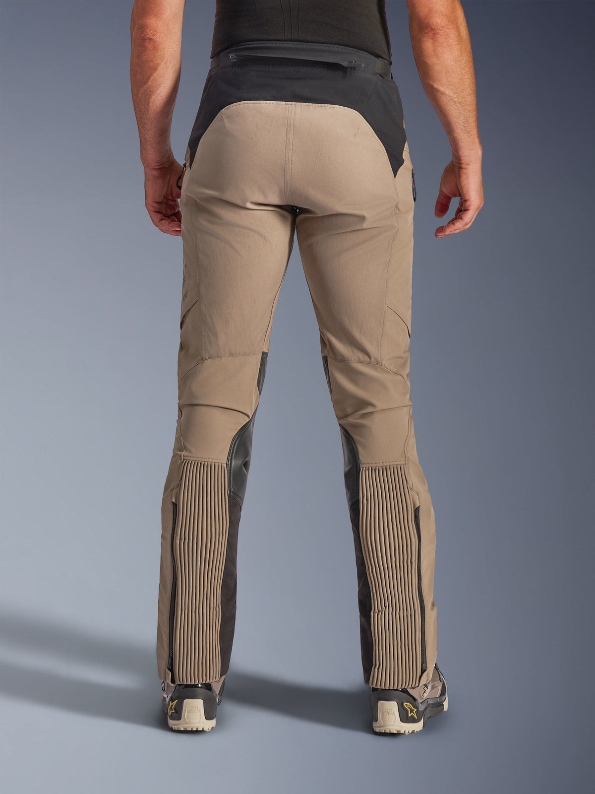 Alpinestars AMT-8 Stretch Drystar® XF Pants, Walnut Black, vista posteriore su modello, telaio in tessuto elasticizzato color tan con sprone in vita e pannelli sui polpacci neri, ampie zone a fisarmonica sulla parte inferiore delle gambe, ingressi gamba con zip e vestibilità adventure-touring