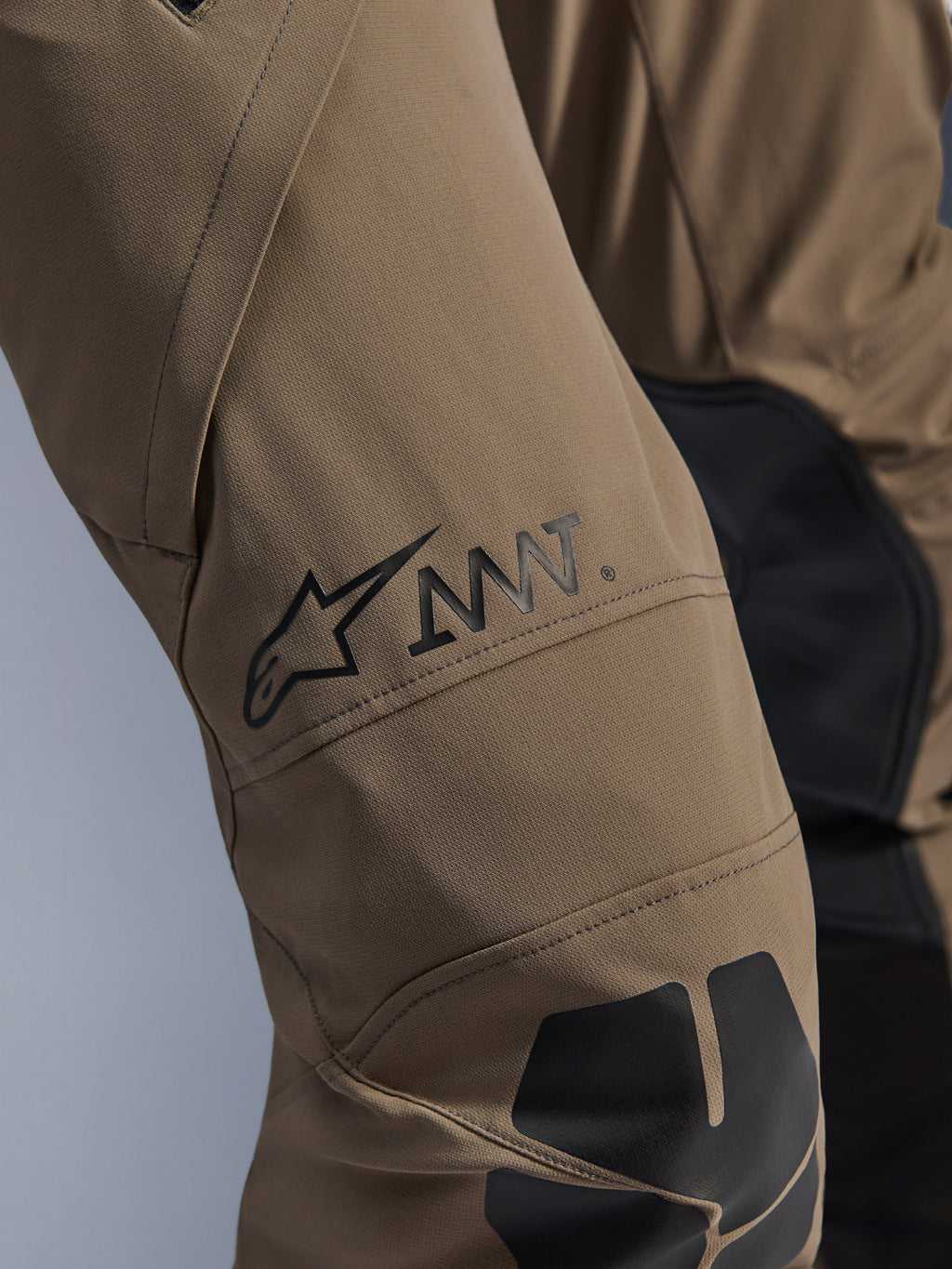 Pantaloni Alpinestars AMT-8 Stretch Drystar® XF in Walnut Black, primo piano della gamba con logo AMT e stella Alpinestars neri, tessuto elasticizzato ad alte prestazioni con inserti neri, abbigliamento tecnico da moto adventure