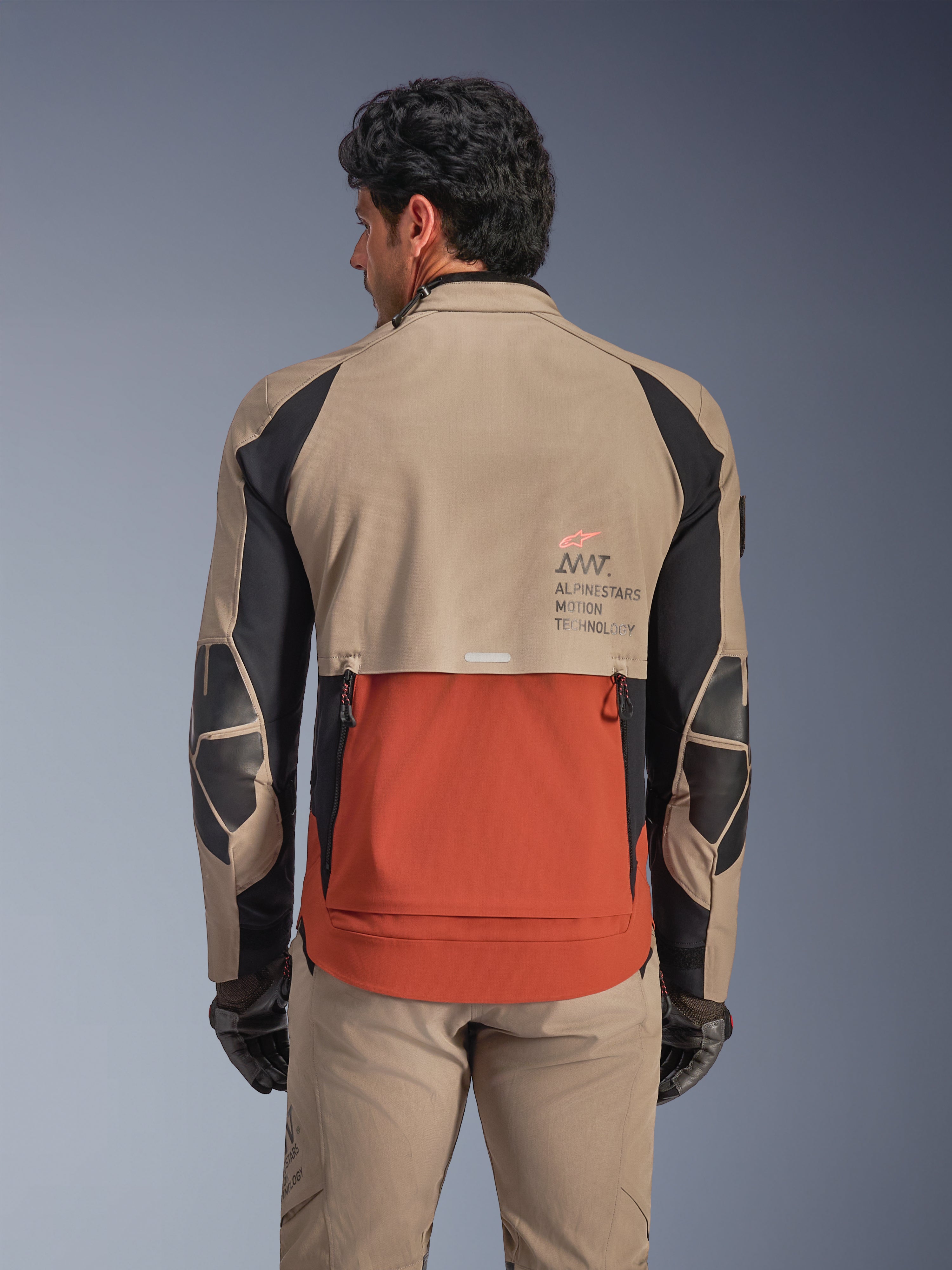 Giacca Alpinestars AMT-8 Stretch Drystar® XF, Walnut Rust Black, vista posteriore su modello, mette in evidenza lo scarico posteriore con design a listelli color ruggine, sezioni superiori color noce, dettagli neri sulle maniche e marchio Alpinestars Motion Technology