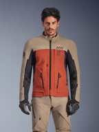 Giacca Alpinestars AMT-8 Stretch Drystar® XF, giacca adventure touring Walnut Rust Black, indossata da un modello uomo con pantaloni e guanti coordinati, caratterizzata da un design tricolore sabbia, ruggine e nero con logo AMT sul petto, vestibilità active touring per la guida in moto