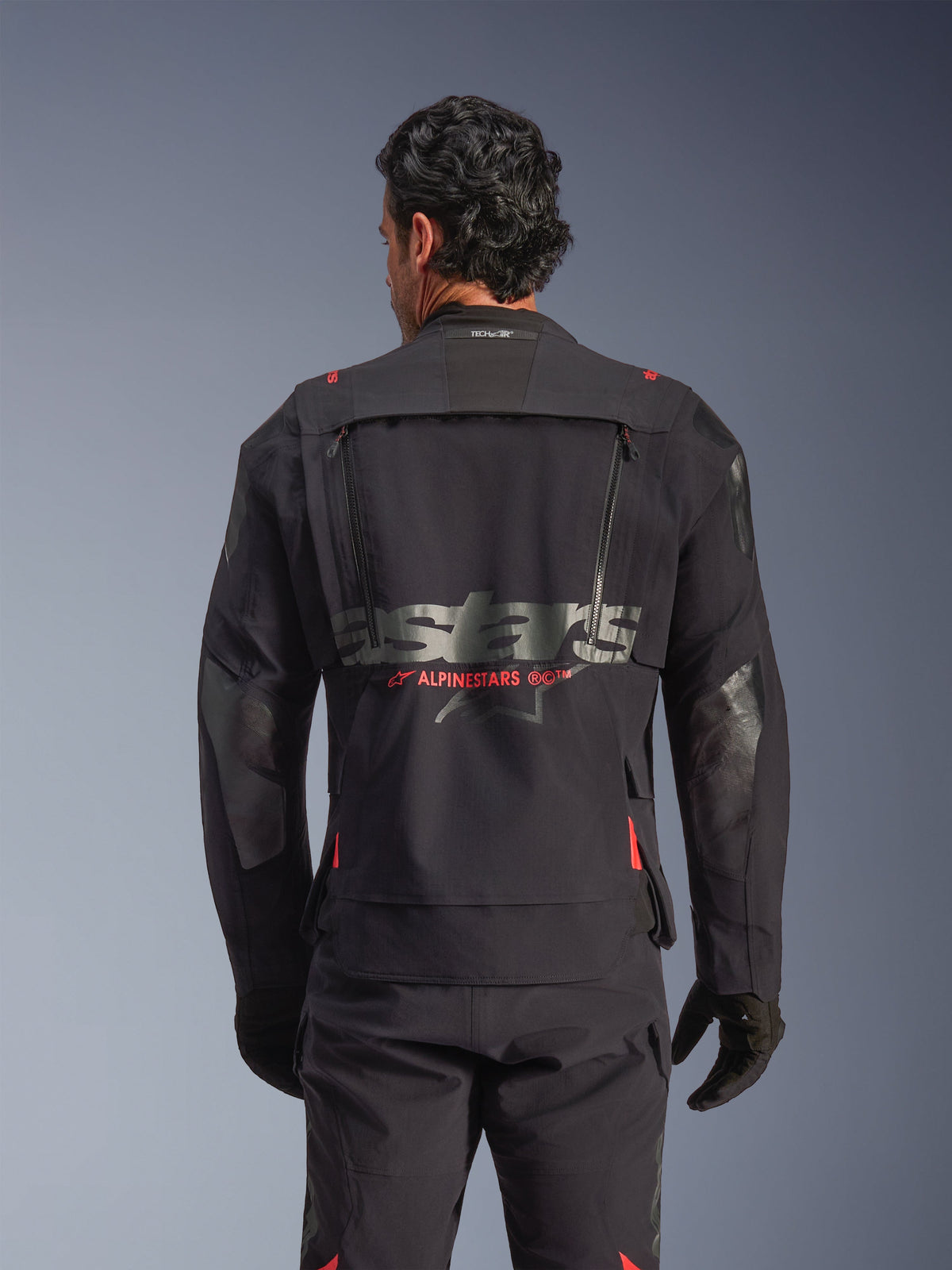 Giacca laminata Alpinestars Halo Pro Drystar® XF in Black Dark Shadow, vista posteriore su modello, che mostra il pannello di ventilazione tecnica posteriore con cerniere, accenti rossi del logo Alpinestars e marchio Tech-Air® sul collo, abbigliamento modulare per adventure riding.
