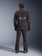Un pilota visto da dietro che indossa la giacca laminata Alpinestars Halo Pro Drystar® XF in Black Dark Shadow, con un grande logo Astars grigio e marchio Alpinestars rosso, pannelli di ventilazione modulari sulla schiena, abbinata a pantaloni da adventure coordinati e stivali neri.