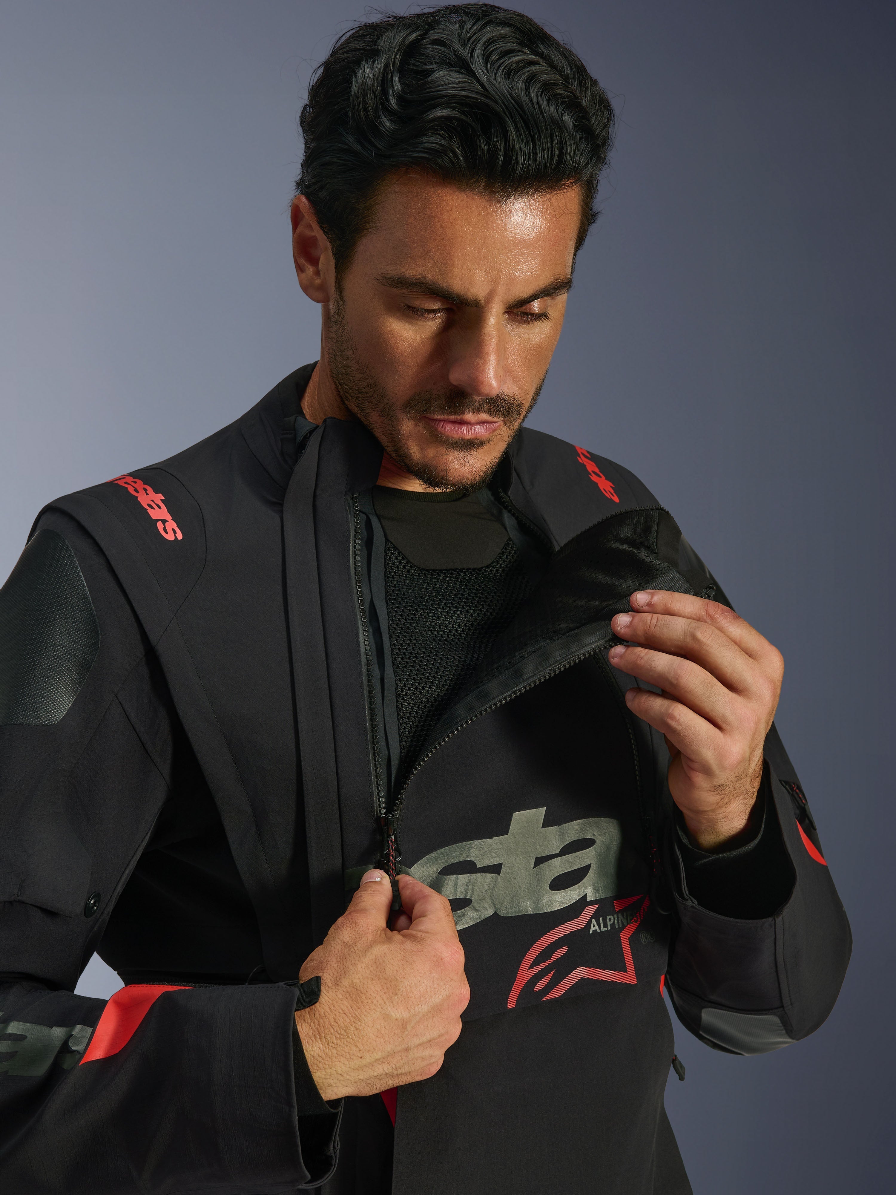 Giacca laminata Alpinestars Halo Pro Drystar® XF, Black Dark Shadow, modello che mostra il sistema di ventilazione modulare aprendo la zip del pannello frontale asimmetrico sul petto, giacca da adventure touring con logo Alpinestars rosso e dettagli in rete tecnica.