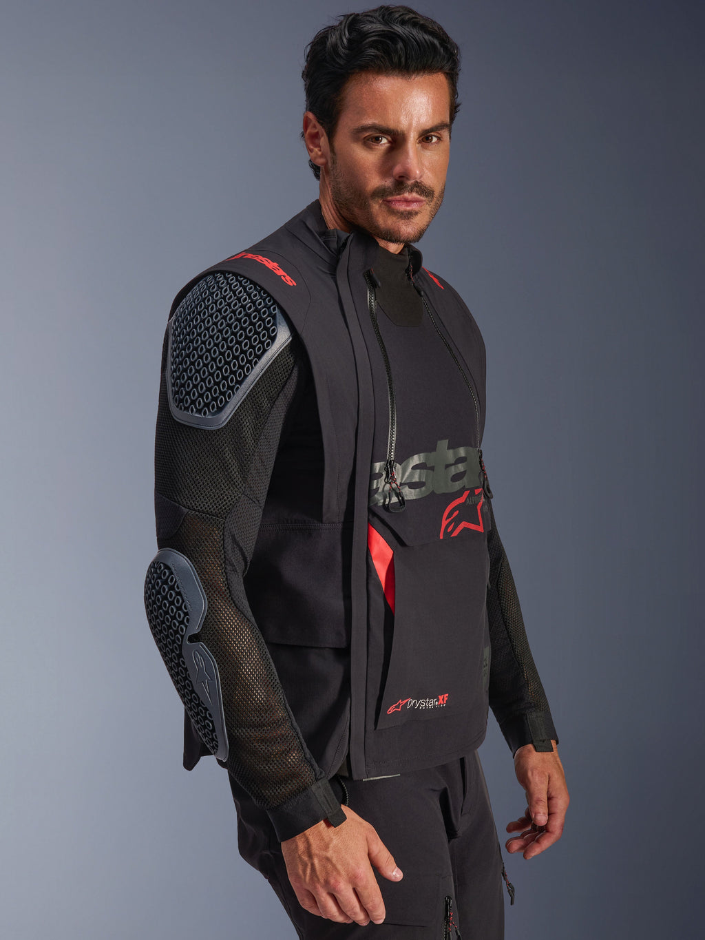 Giacca laminata Alpinestars Halo Pro Drystar® XF, nero e Dark Shadow, giacca da moto adventure indossata da un modello, configurazione modulare con maniche in rete e protezioni integrate per spalle e gomiti, accenti del logo rossi e cerniere tecniche impermeabili.