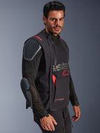 Giacca laminata Alpinestars Halo Pro Drystar® XF, nero e Dark Shadow, giacca da moto adventure indossata da un modello, configurazione modulare con maniche in rete e protezioni integrate per spalle e gomiti, accenti del logo rossi e cerniere tecniche impermeabili.