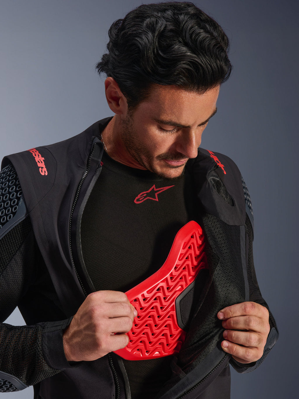Alpinestars Halo Pro Drystar® XF Laminated Jacket in Black Dark Shadow, indossata da un modello e aperta per mostrare la protezione per il petto Nucleon Flex Pro rossa, giacca tecnica da moto con armatura integrata, abbigliamento per guida adventure.