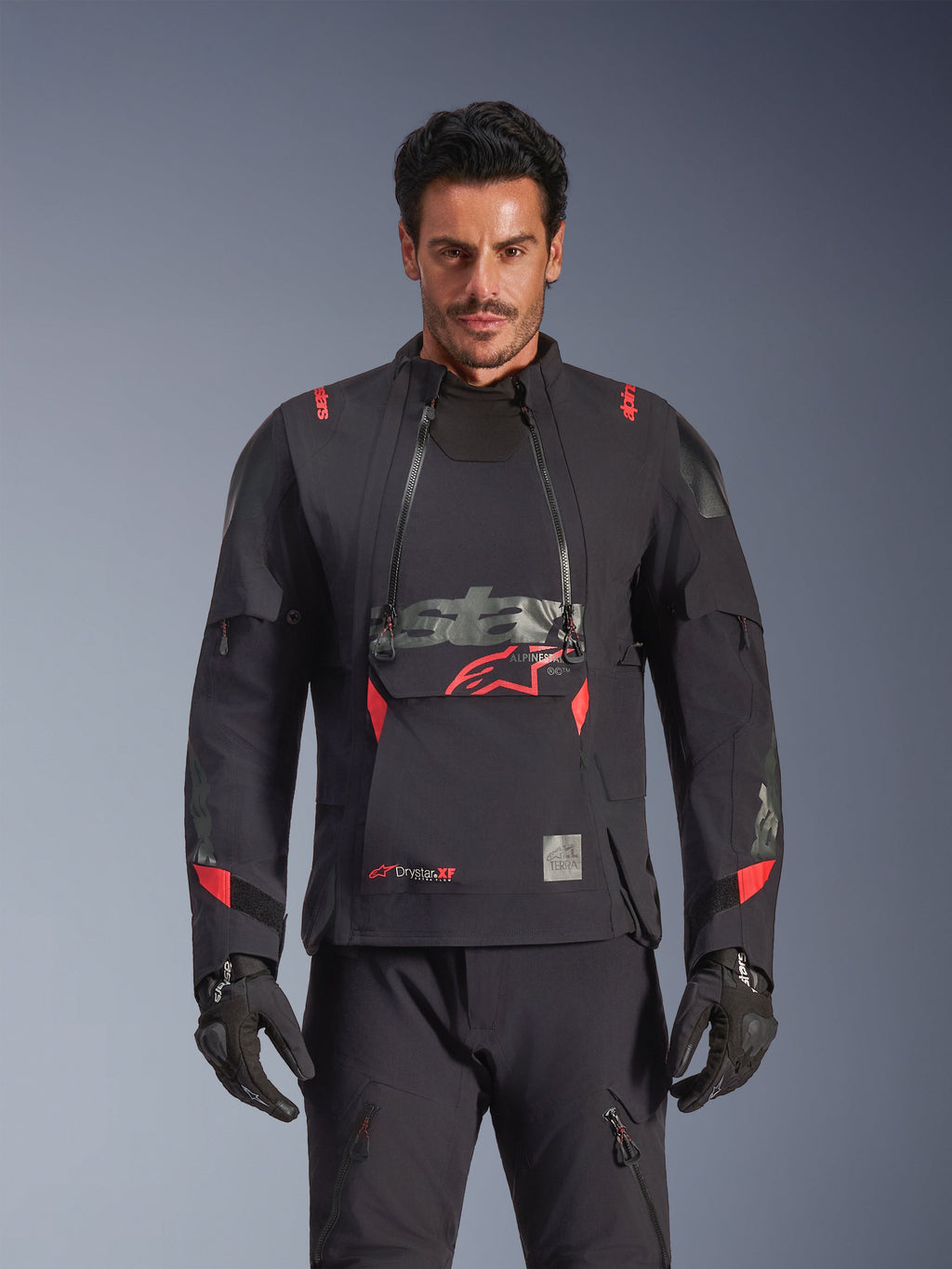 Giacca Alpinestars Halo Pro Drystar® XF Laminated, giacca da moto adventure, colore Black Dark Shadow con accenti rossi, modello che indossa l'equipaggiamento tecnico completo con guanti e pantaloni coordinati, vista frontale che evidenzia i pannelli di ventilazione modulari sul petto e la costruzione impermeabile.
