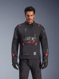 Giacca Alpinestars Halo Pro Drystar® XF Laminated, giacca da moto adventure, colore Black Dark Shadow con accenti rossi, modello che indossa l'equipaggiamento tecnico completo con guanti e pantaloni coordinati, vista frontale che evidenzia i pannelli di ventilazione modulari sul petto e la costruzione impermeabile.