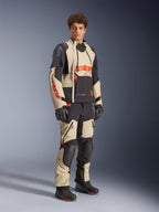 Modello che indossa la giacca Alpinestars Halo Pro Drystar® XF Laminated in Mastic Black, con pannelli beige e neri e accenti rossi, abbinata a pantaloni adventure coordinati e guanti neri, progettata per la guida motociclistica adventure su ogni terreno.