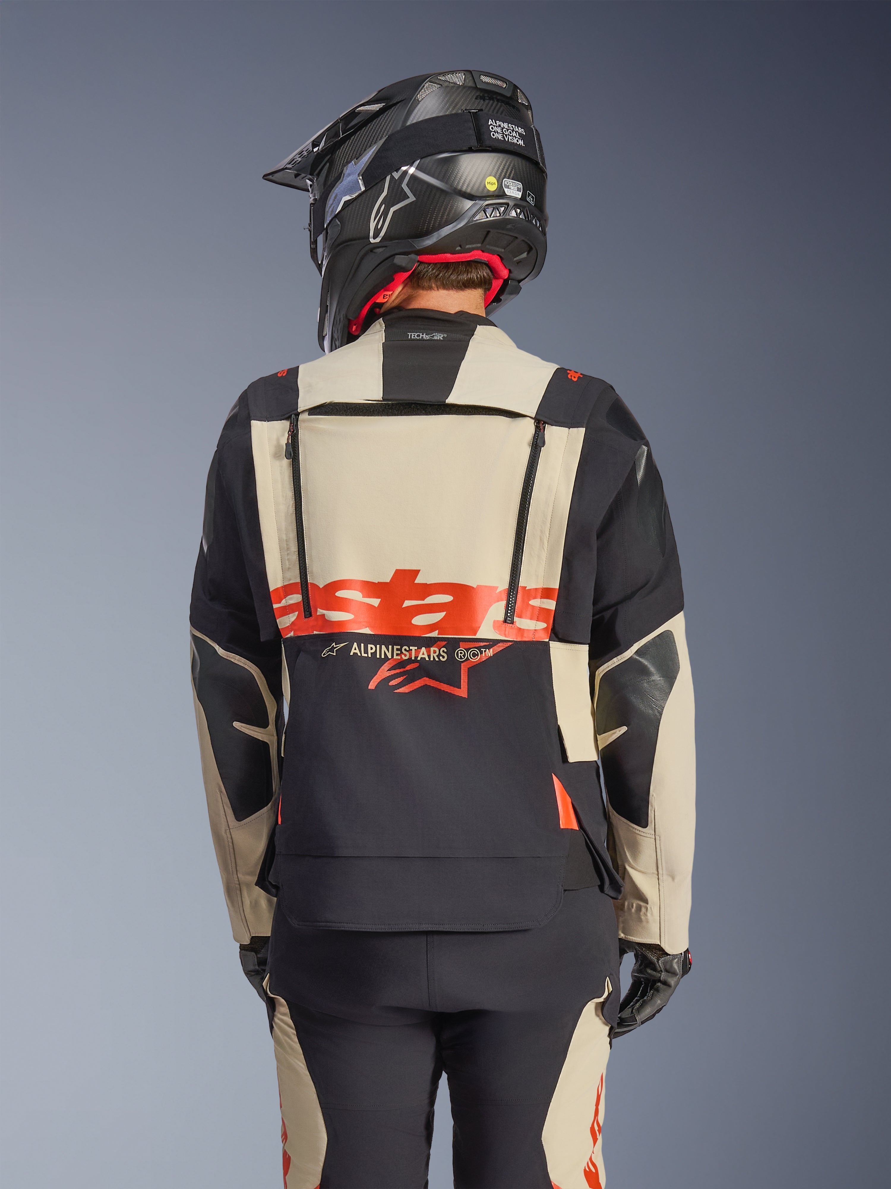 Giacca laminata Alpinestars Halo Pro Drystar® XF in Mastic Black, vista posteriore che mostra il pannello posteriore modulare con logo rosso e cerniere di ventilazione, indossata da un pilota con pantaloni adventure coordinati e casco nero