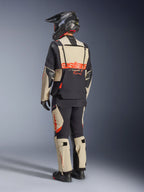 Giacca laminata Alpinestars Halo Pro Drystar® XF, Mastic Black, vista posteriore di un pilota che indossa la tuta completa da moto adventure con pantaloni coordinati, casco adventure nero e stivali, con un grande logo Alpinestars rosso sulla schiena.
