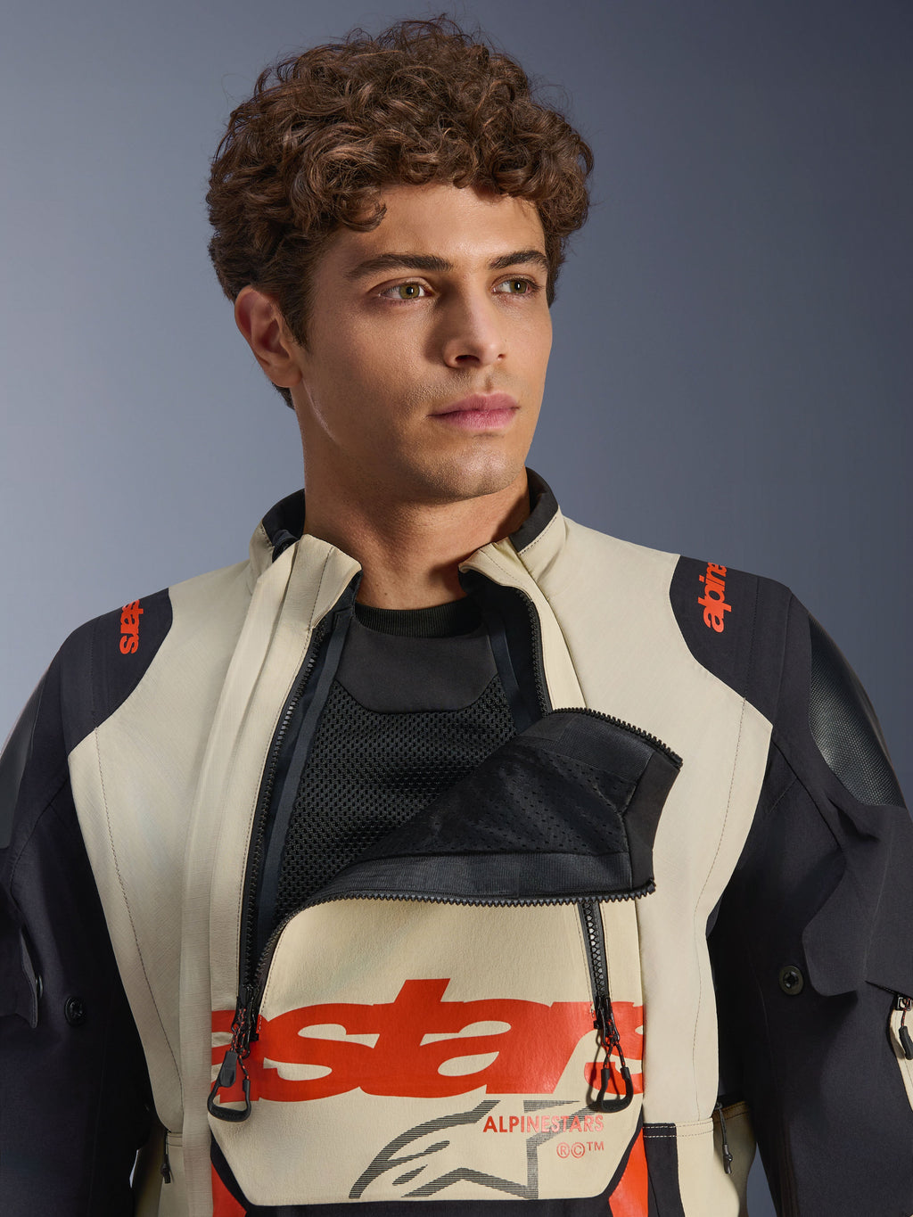 Giacca laminata Alpinestars Halo Pro Drystar® XF in Mastic Black, modello uomo che indossa la giacca con il pannello di ventilazione frontale aperto per mostrare lo strato in rete sottostante, logo rosso e pannelli neri sulle spalle, abbigliamento tecnico da moto adventure