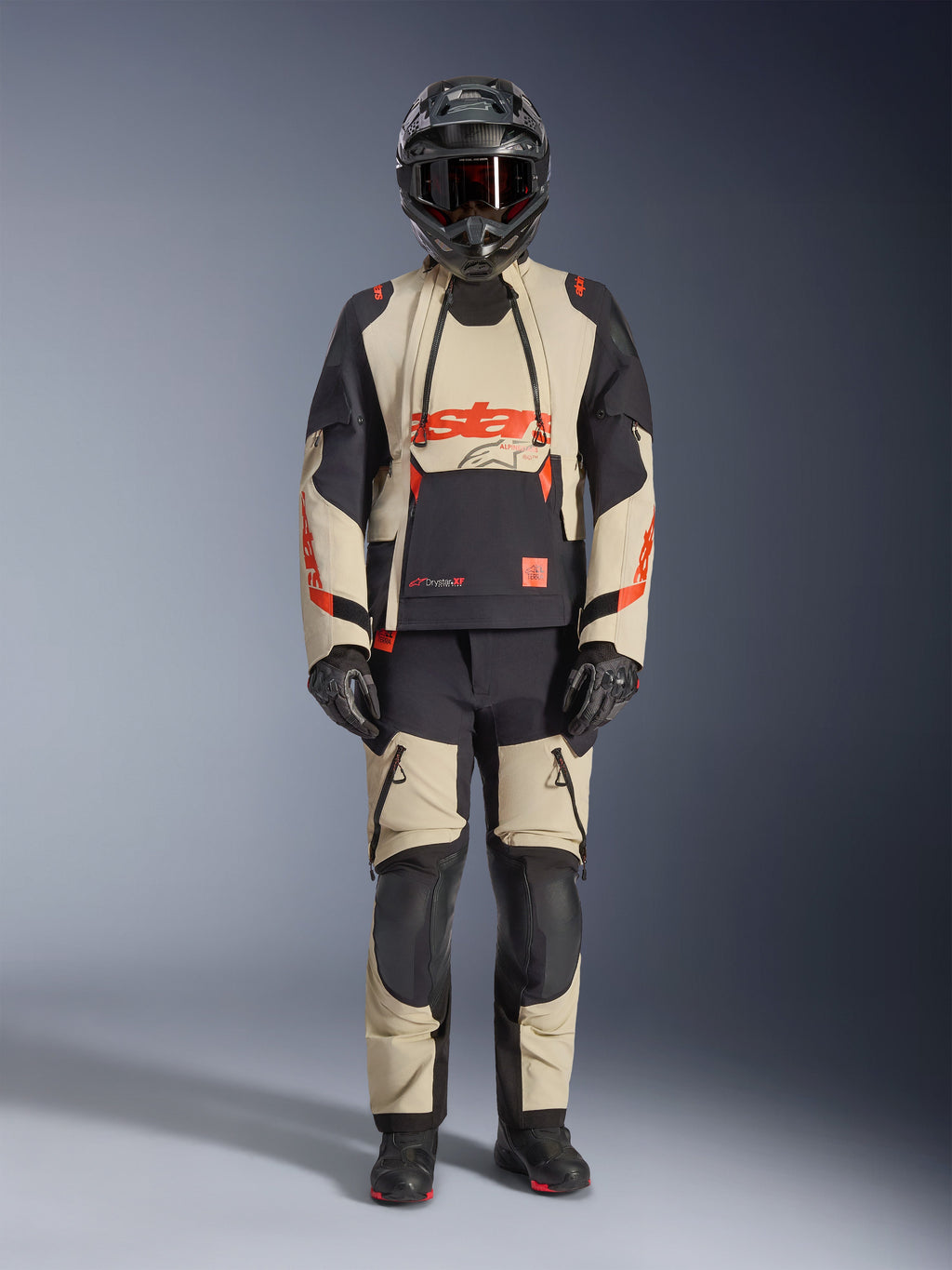 Giacca laminata Alpinestars Halo Pro Drystar® XF, giacca da moto adventure, Mastic Black, beige e nero con accenti arancioni, indossata con pantaloni coordinati, casco e guanti, design tecnico con cerniere impermeabili e pannelli modulari per guida su strada e fuoristrada
