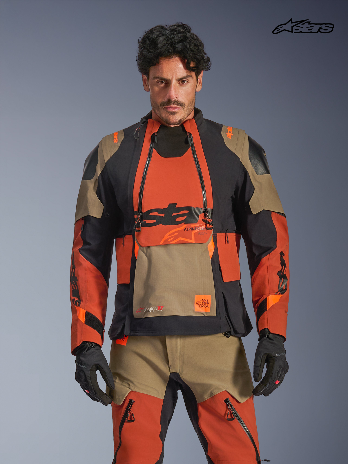 Giacca Alpinestars Halo Pro Drystar XF Laminata, giacca da moto adventure da uomo in marrone noce, ruggine e nero, vista frontale su un modello che indossa attrezzatura coordinata, con costruzione impermeabile e pannelli di ventilazione modulari