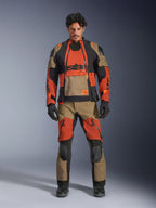 Modello che indossa la giacca laminata Alpinestars Halo Pro Drystar® XF e pantaloni coordinati nella colorazione Walnut Rust Black, abbigliamento modulare da moto adventure con pannelli di ventilazione frontali e cerniere, completato da guanti e stivali da moto neri.