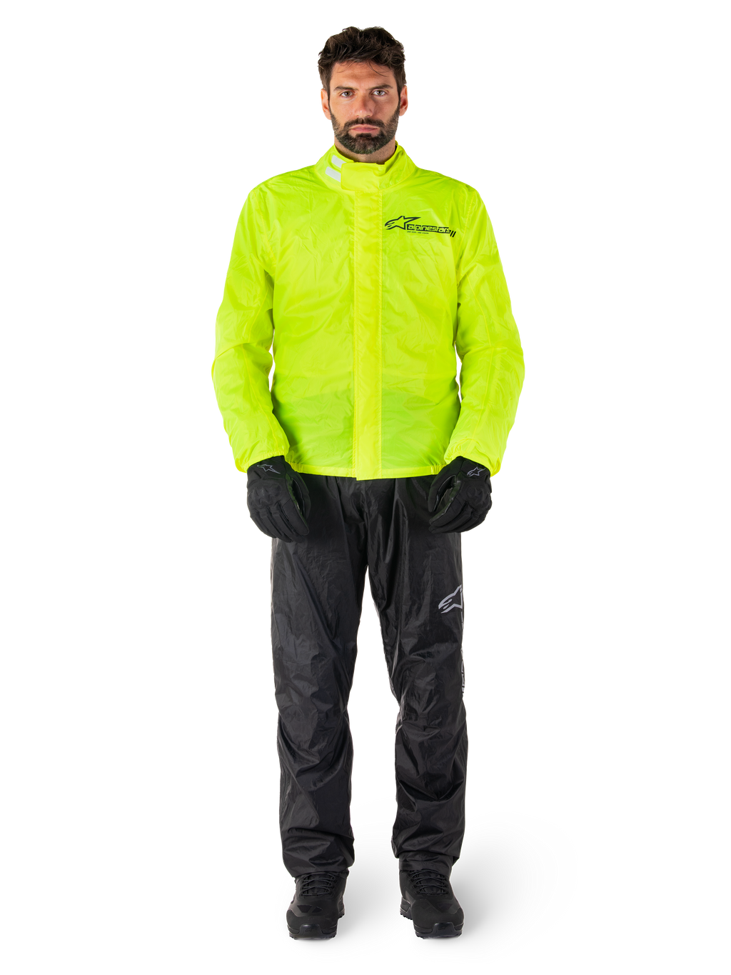 Giacca e pantaloni Alpinestars Hurricane Rain V2, giallo neon e nero, tuta antipioggia da moto impermeabile indossata con guanti e stivali neri, con il logo Alpinestars sul petto e sulla gamba