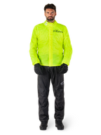 Giacca e pantaloni Alpinestars Hurricane Rain V2, giallo neon e nero, tuta antipioggia da moto impermeabile indossata con guanti e stivali neri, con il logo Alpinestars sul petto e sulla gamba