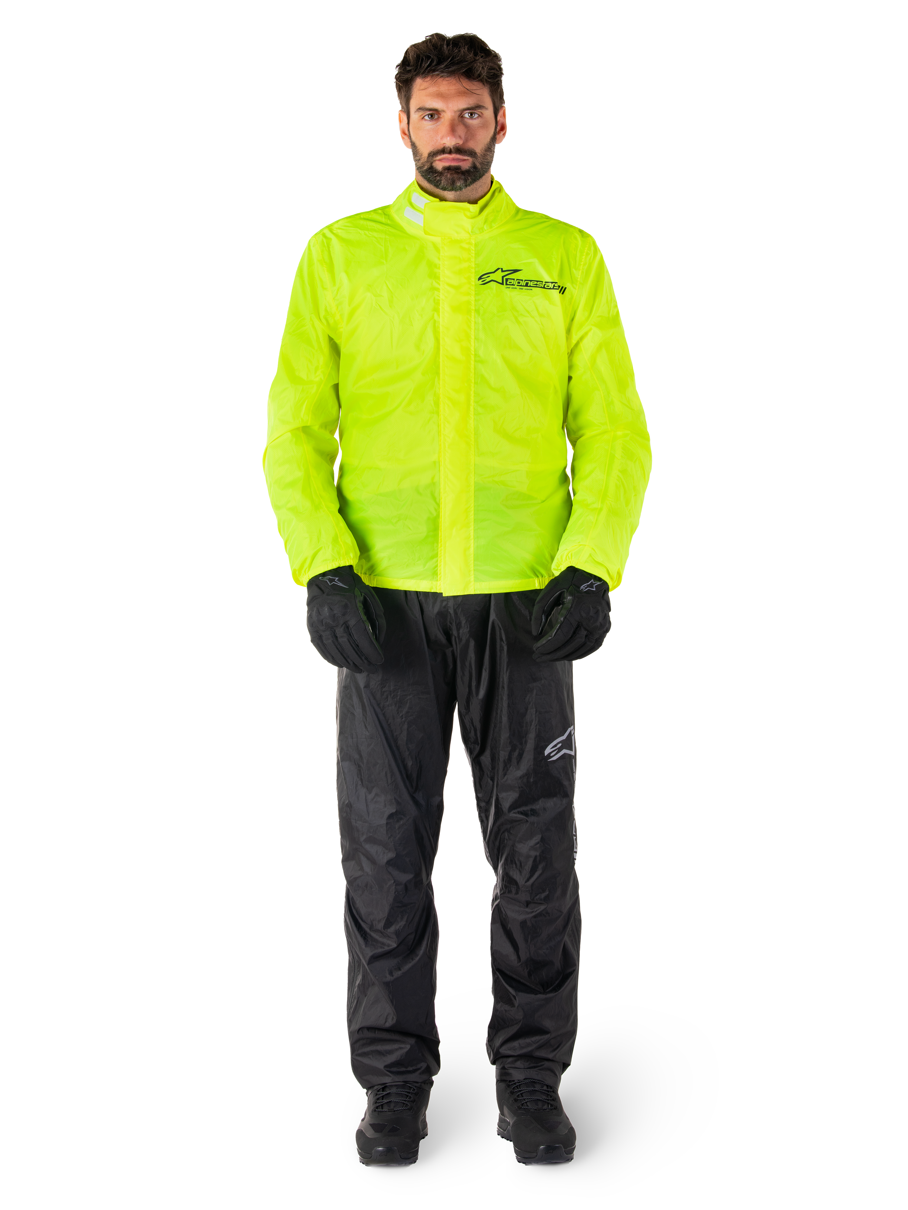 Giacca e pantaloni Alpinestars Hurricane Rain V2, giallo neon e nero, tuta antipioggia da moto impermeabile indossata con guanti e stivali neri, con il logo Alpinestars sul petto e sulla gamba