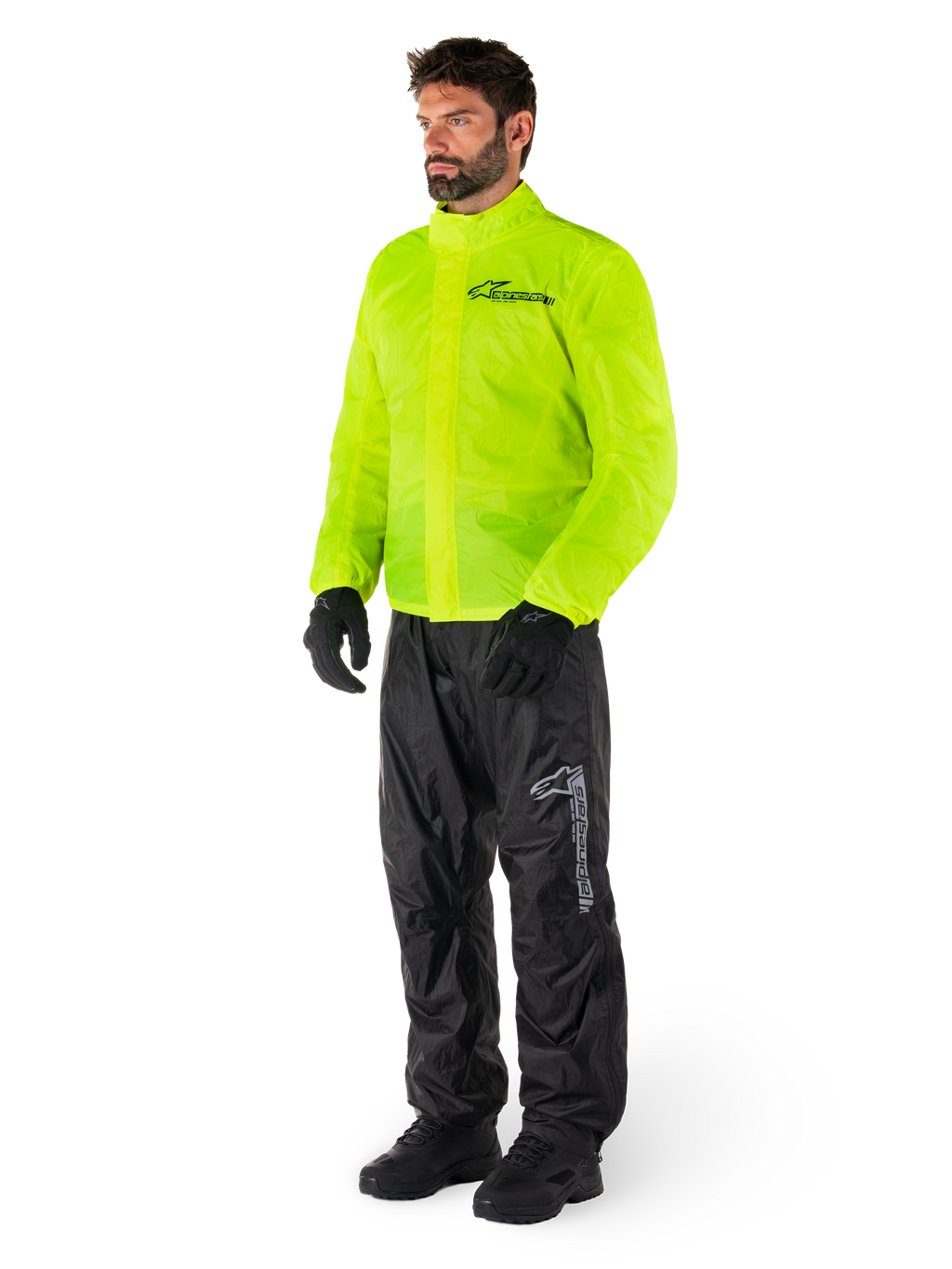 Uomo che indossa la giacca Alpinestars Hurricane Rain V2 in Giallo Fluo e i pantaloni Hurricane Rain V2 neri, abbigliamento antipioggia da moto impermeabile e ad alta visibilità, con loghi riflettenti su petto e coscia, outfit completo con guanti e stivali neri.