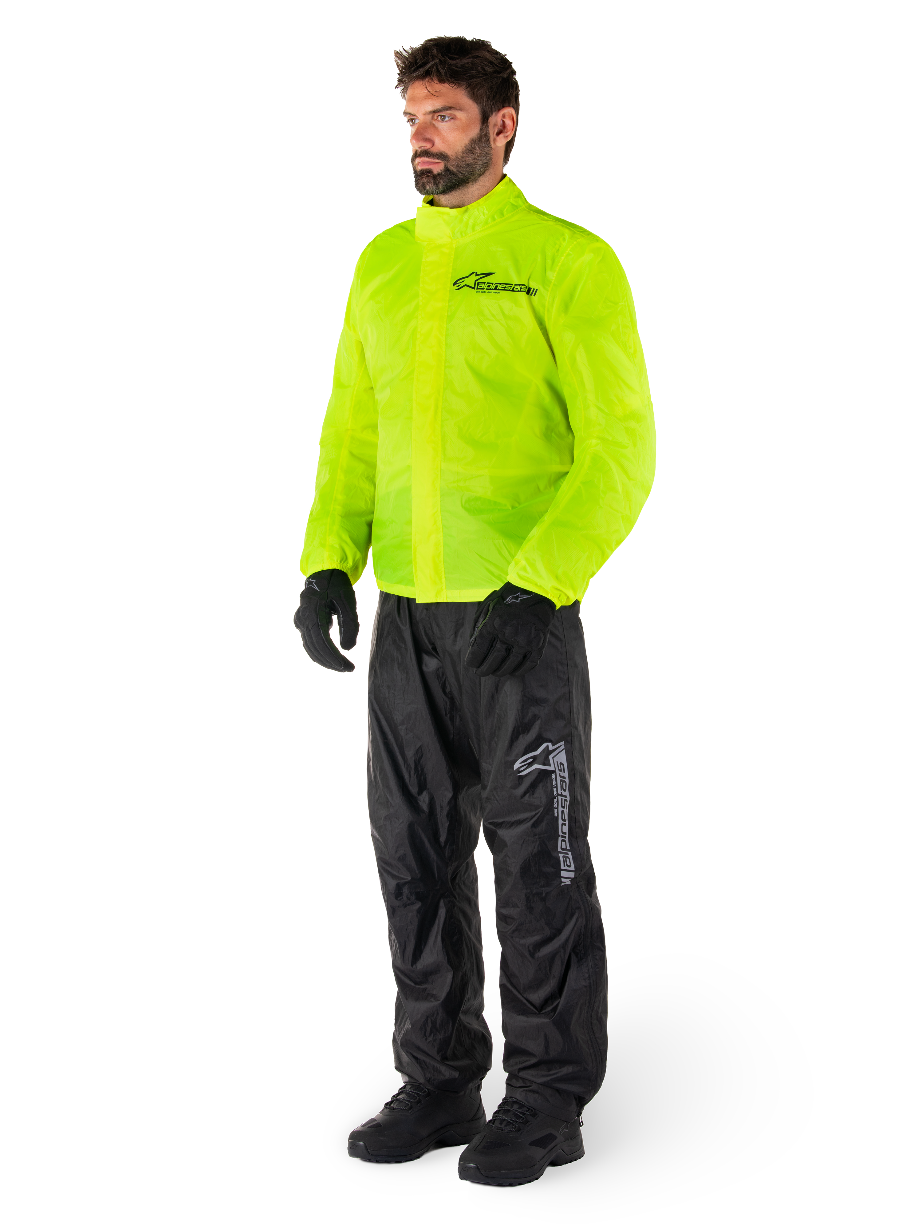 Uomo che indossa la giacca Alpinestars Hurricane Rain V2 in Giallo Fluo e i pantaloni Hurricane Rain V2 neri, abbigliamento antipioggia da moto impermeabile e ad alta visibilità, con loghi riflettenti su petto e coscia, outfit completo con guanti e stivali neri.