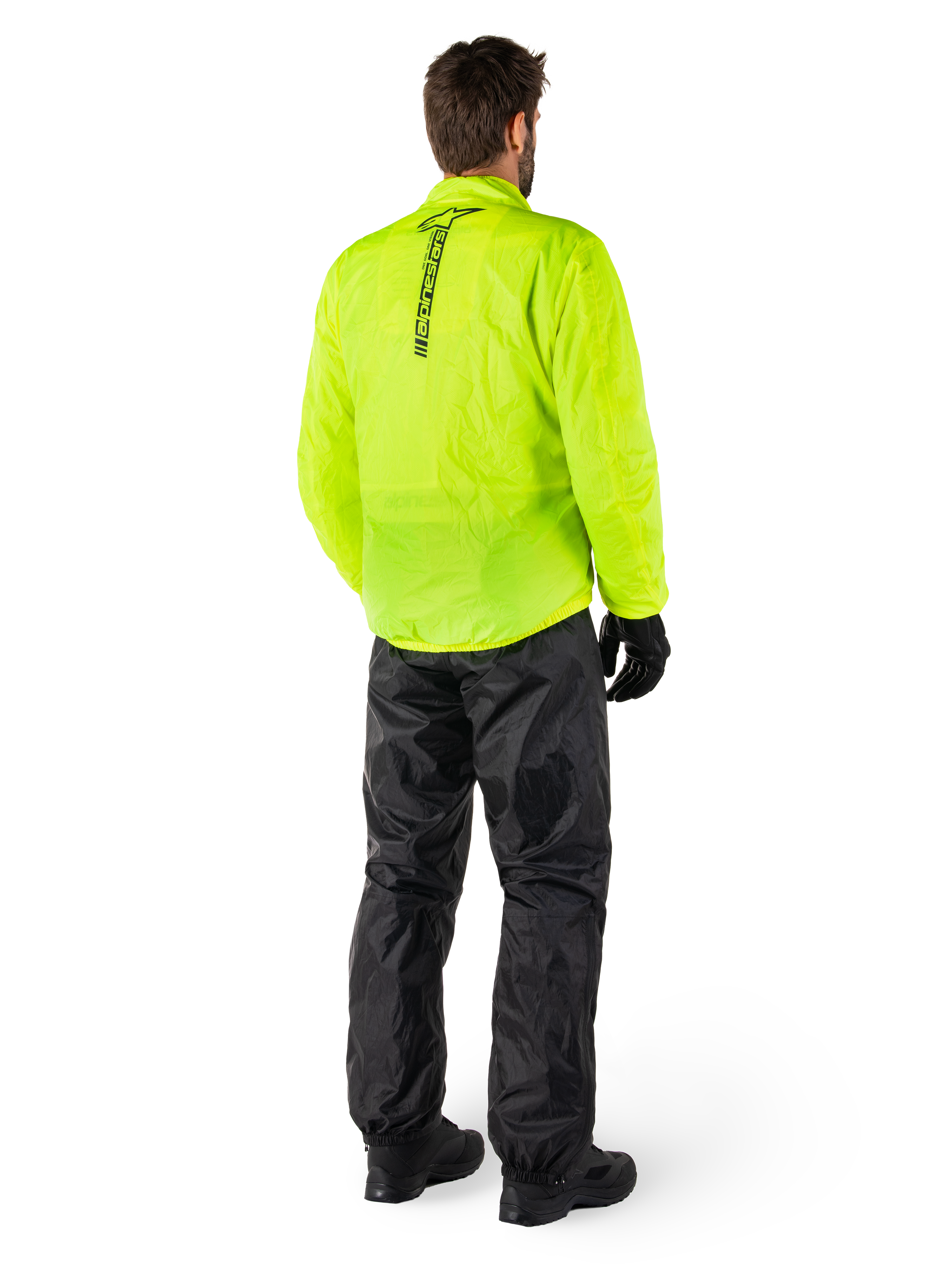 Persona vista di schiena che indossa la giacca Alpinestars Hurricane Rain V2 in Giallo Fluo e i pantaloni Hurricane Rain V2 neri, logo verticale sul retro della giacca, abbigliamento antipioggia impermeabile da moto con guanti e stivali neri