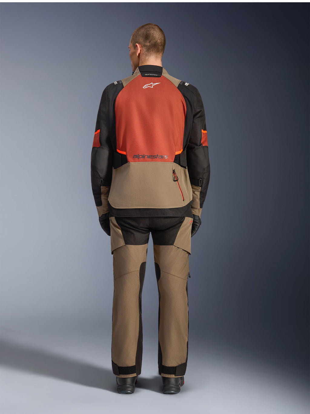 Alpinestars Giacca Andes V4 Drystar®, Walnut Rust Black, vista posteriore di giacca da moto touring con pannello superiore della schiena color ruggine e parte inferiore noce, indossata con pantaloni adventure abbinati e stivali neri