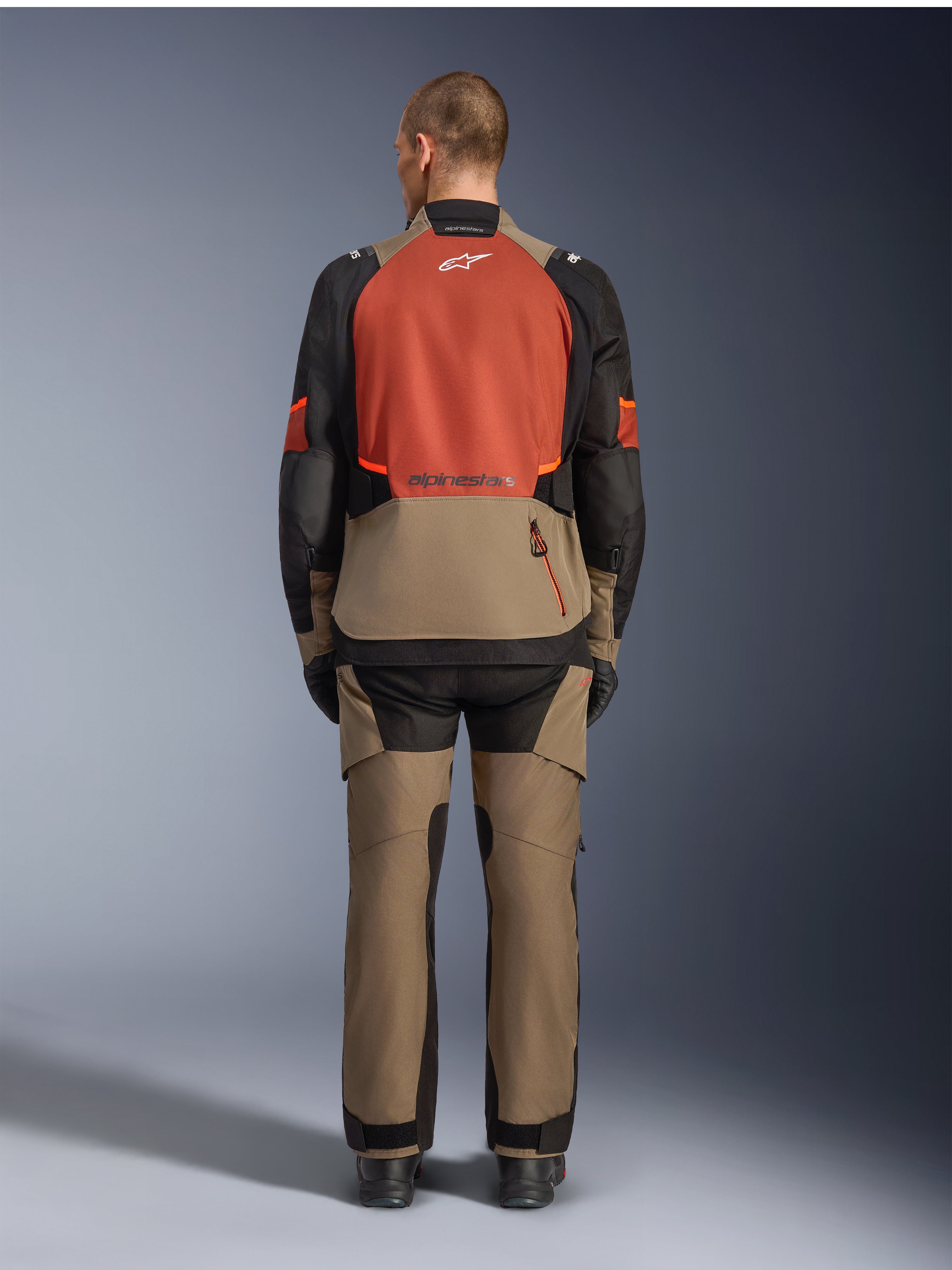 Alpinestars Giacca Andes V4 Drystar®, Walnut Rust Black, vista posteriore di giacca da moto touring con pannello superiore della schiena color ruggine e parte inferiore noce, indossata con pantaloni adventure abbinati e stivali neri