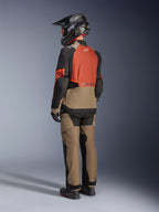 Giacca Alpinestars Andes V4 Drystar®, colorazione Walnut Rust Black, vista posteriore di un pilota che indossa pantaloni adventure coordinati, casco nero e stivali da moto neri, abbigliamento tecnico da moto in tessuto per adventure touring in ogni condizione atmosferica.