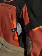 Giacca Alpinestars Andes V4 Drystar®, Walnut Rust Black, primo piano della presa d'aria diretta con fodera in rete, materiale tessile resistente con accenti arancioni, dettaglio del bottone a pressione e del logo Alpinestars