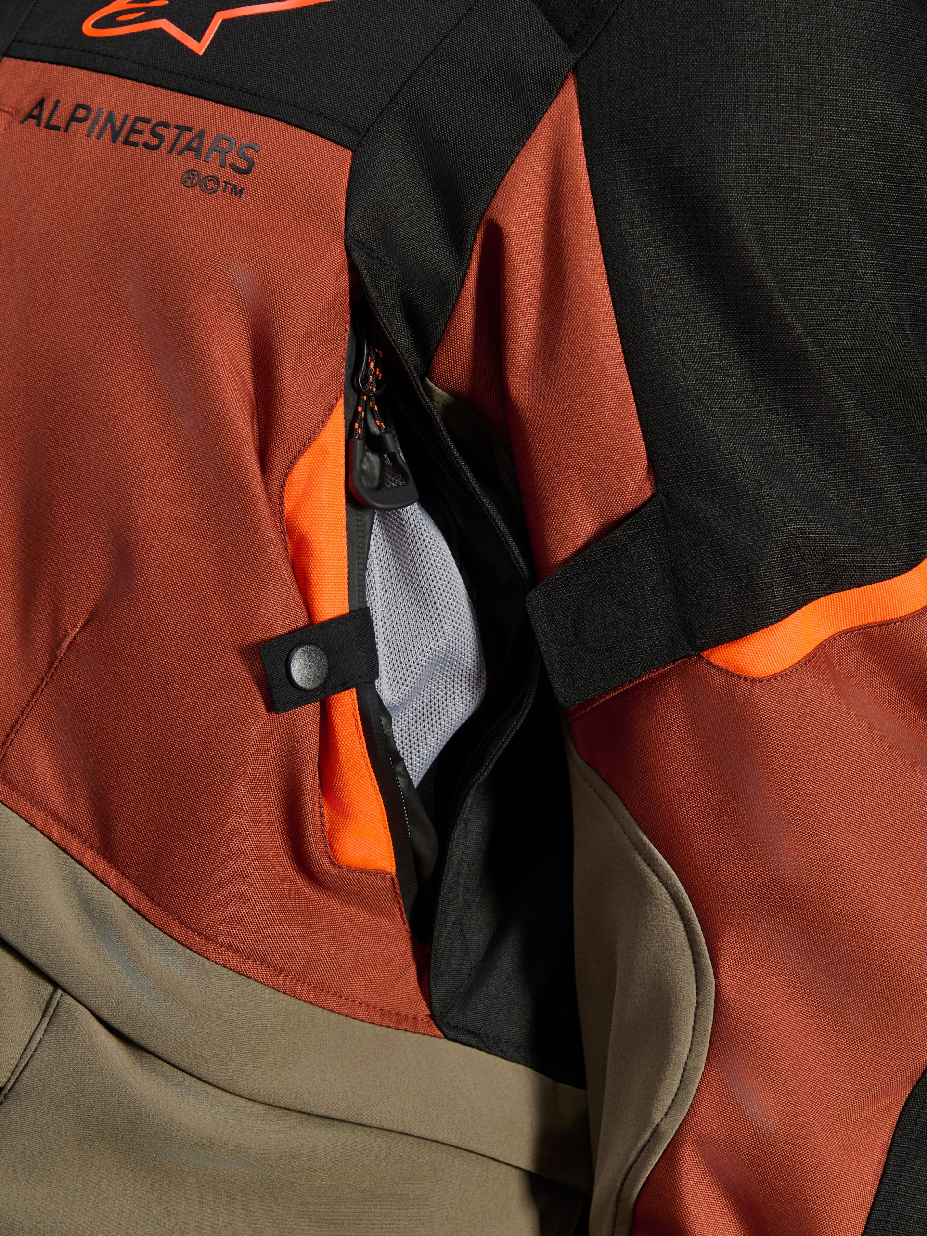 Giacca Alpinestars Andes V4 Drystar®, Walnut Rust Black, primo piano della presa d'aria diretta con fodera in rete, materiale tessile resistente con accenti arancioni, dettaglio del bottone a pressione e del logo Alpinestars